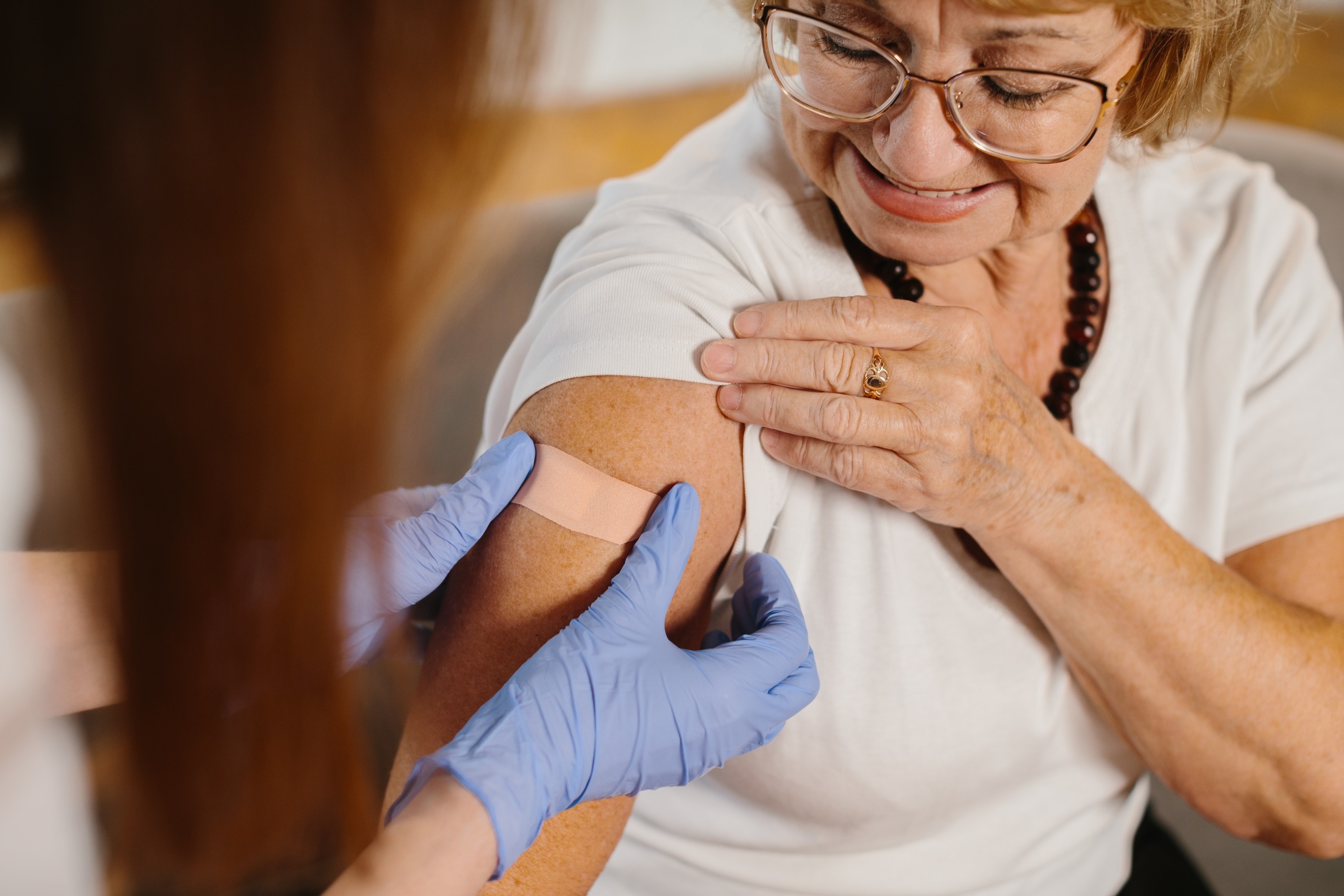 A woman smiles as a nurse checks her arm after receiving a vaccine shot.